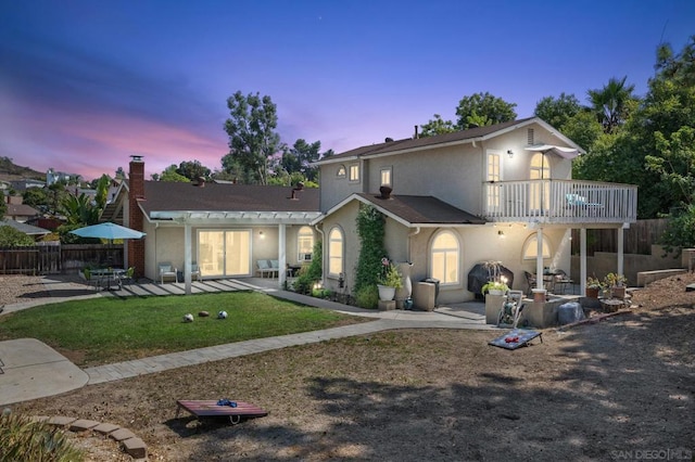 back house at dusk featuring a yard, a balcony, and a patio