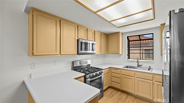 kitchen with appliances with stainless steel finishes, sink, light brown cabinets, and light hardwood / wood-style floors