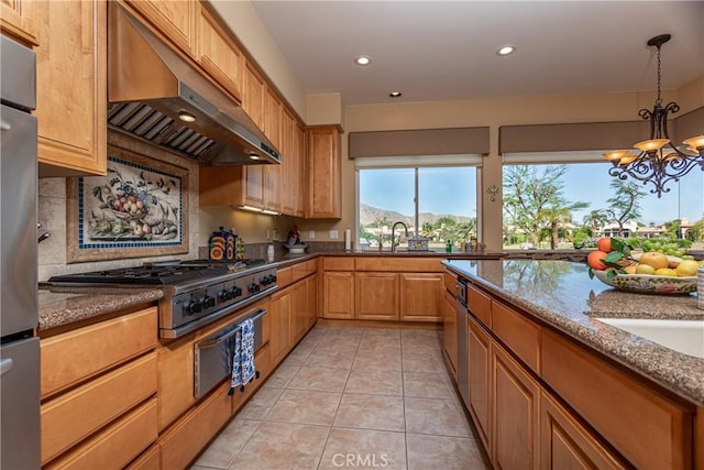 kitchen featuring hanging light fixtures, an inviting chandelier, light stone counters, range hood, and stainless steel gas stovetop