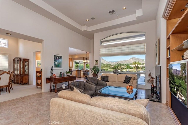 living room featuring a mountain view, an inviting chandelier, a towering ceiling, a tray ceiling, and light tile patterned flooring