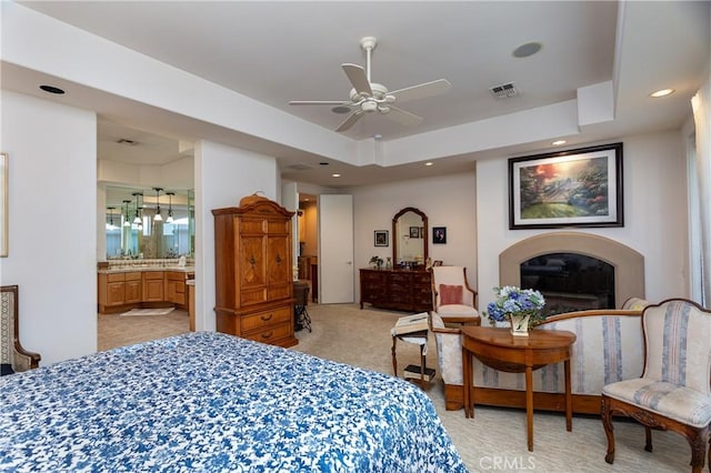 carpeted bedroom with a tray ceiling, connected bathroom, and ceiling fan