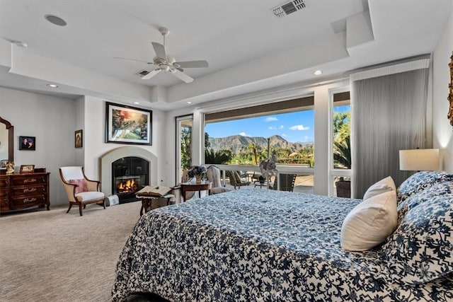 carpeted bedroom featuring a mountain view, a raised ceiling, and ceiling fan