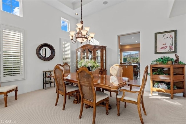 carpeted dining space with a towering ceiling and an inviting chandelier