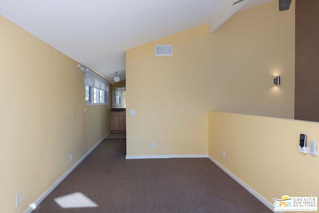 spare room featuring lofted ceiling and dark colored carpet