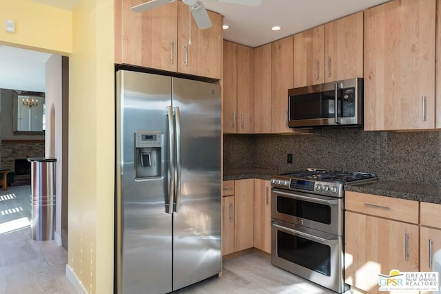 kitchen with appliances with stainless steel finishes, backsplash, ceiling fan, light hardwood / wood-style flooring, and dark stone countertops