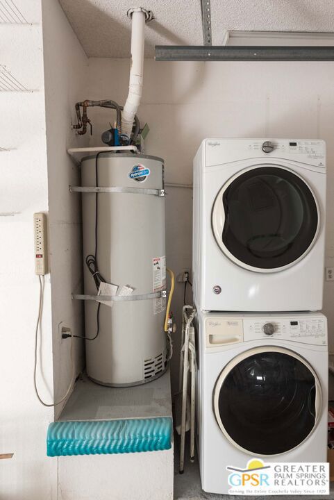 laundry room featuring water heater, stacked washer and dryer, and a textured ceiling