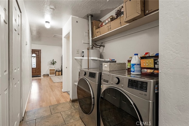 washroom with a textured ceiling, light wood-type flooring, water heater, and washing machine and dryer