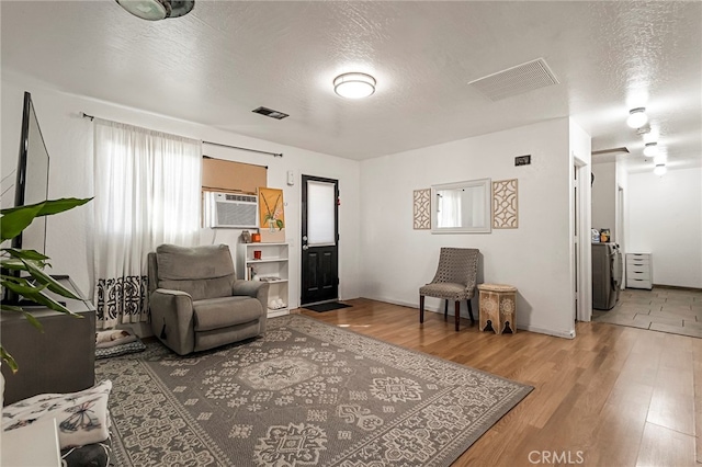 living room featuring wood-type flooring, a textured ceiling, washer / dryer, and a wall unit AC