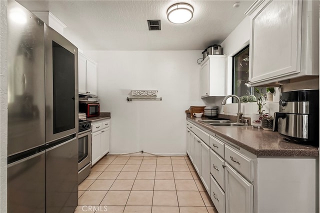 kitchen with light tile patterned floors, appliances with stainless steel finishes, sink, and white cabinetry