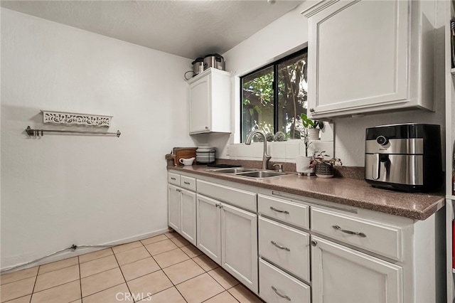 kitchen featuring light tile patterned floors, white cabinets, a textured ceiling, and sink