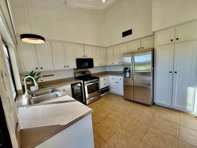 kitchen with appliances with stainless steel finishes, sink, a towering ceiling, and light tile patterned flooring