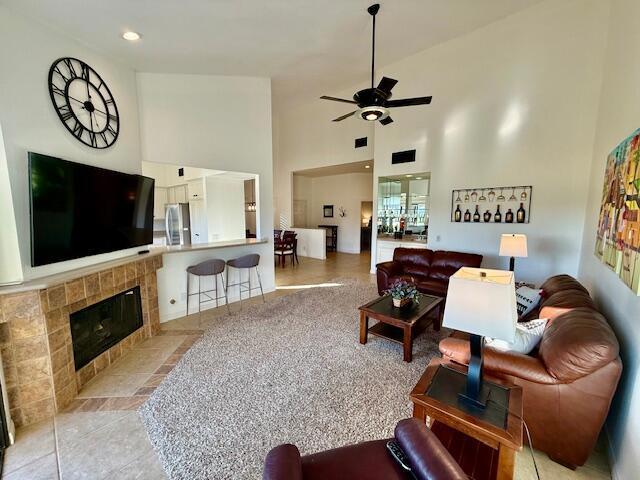 living room featuring a high ceiling, ceiling fan, light tile patterned floors, and a tiled fireplace