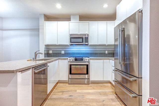 kitchen featuring white cabinets, decorative backsplash, stainless steel appliances, and light hardwood / wood-style flooring