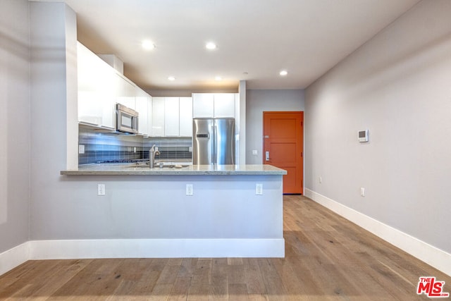 kitchen featuring kitchen peninsula, white cabinetry, light hardwood / wood-style flooring, and stainless steel appliances