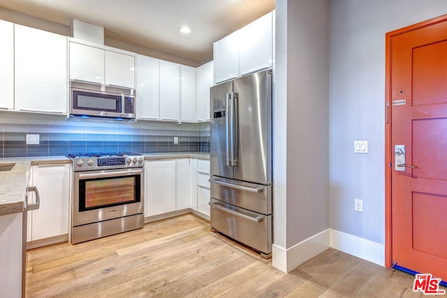 kitchen with tasteful backsplash, white cabinets, light hardwood / wood-style floors, and appliances with stainless steel finishes