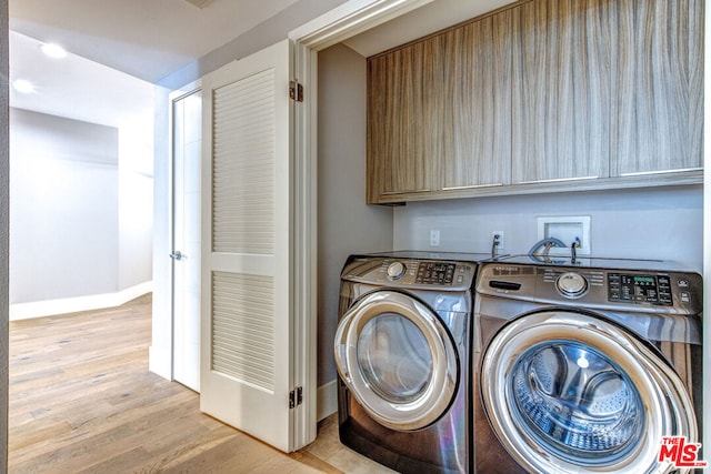 washroom featuring washing machine and dryer, cabinets, and light wood-type flooring