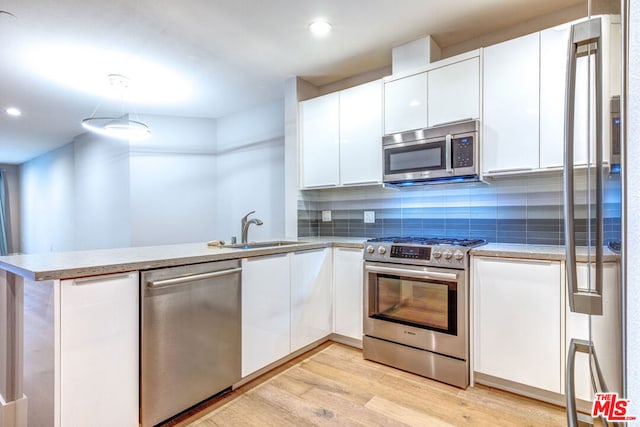 kitchen with pendant lighting, sink, light wood-type flooring, white cabinetry, and stainless steel appliances