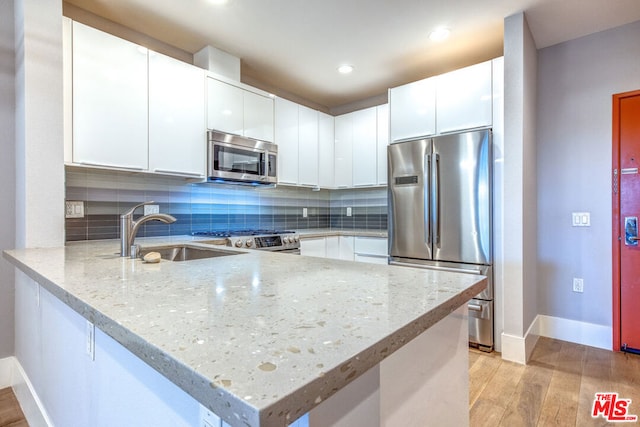 kitchen with kitchen peninsula, light wood-type flooring, stainless steel appliances, sink, and white cabinets