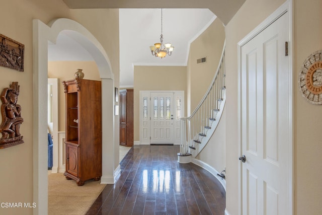 entryway featuring a towering ceiling, ornamental molding, dark hardwood / wood-style flooring, and a notable chandelier