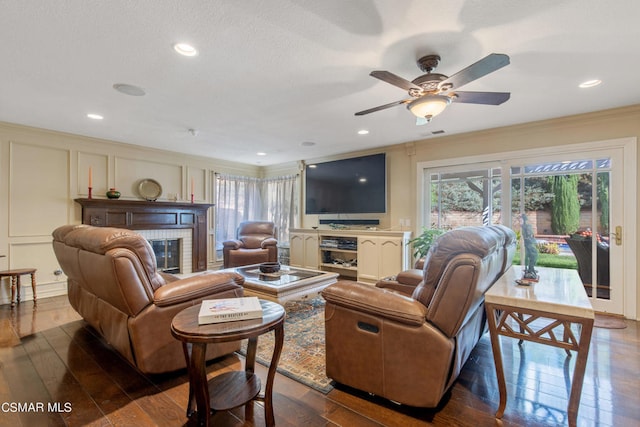 living room featuring hardwood / wood-style flooring, ceiling fan, crown molding, and a brick fireplace