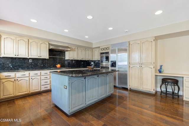 kitchen with a center island, exhaust hood, dark stone counters, dark hardwood / wood-style flooring, and stainless steel appliances