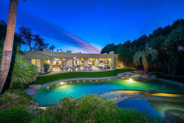 pool at dusk with ceiling fan, a patio area, and an in ground hot tub