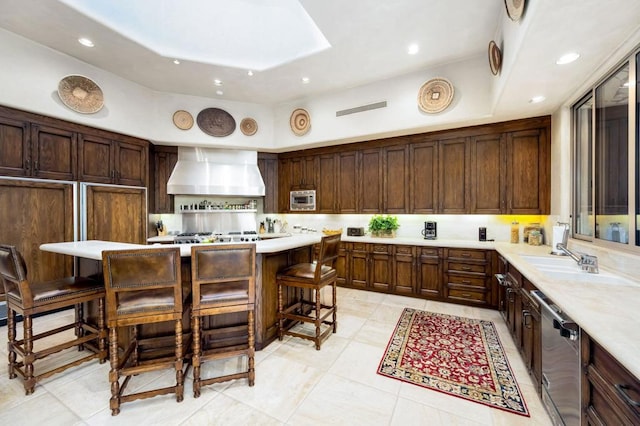 kitchen with wall chimney exhaust hood, dark brown cabinetry, stainless steel appliances, a center island, and a breakfast bar area