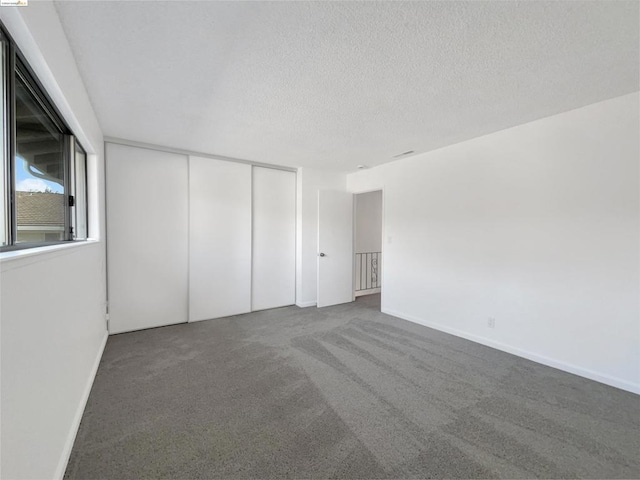 unfurnished room featuring a textured ceiling and dark colored carpet