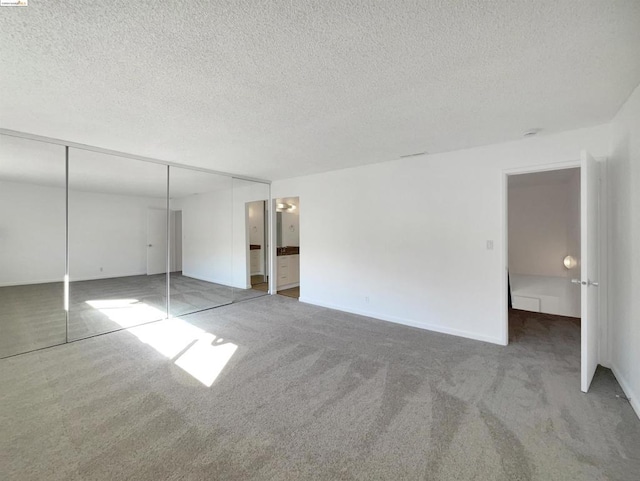 unfurnished bedroom with a textured ceiling, a closet, carpet floors, and ensuite bath