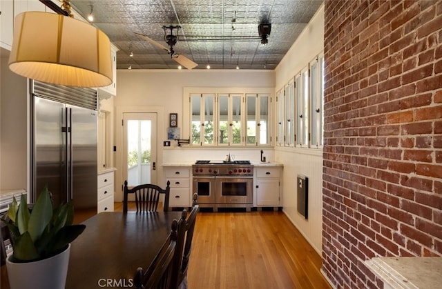 kitchen featuring brick wall, white cabinets, high quality appliances, and light hardwood / wood-style flooring