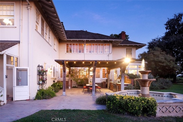 back house at dusk featuring a patio and a balcony