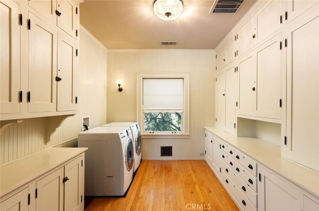 clothes washing area with wooden walls, washer and dryer, cabinets, crown molding, and light hardwood / wood-style floors