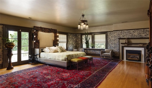 bedroom with a notable chandelier, hardwood / wood-style floors, access to exterior, and multiple windows