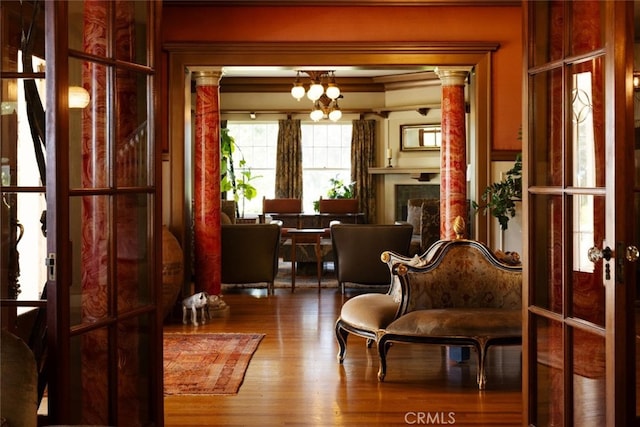 living area with decorative columns, hardwood / wood-style flooring, and crown molding