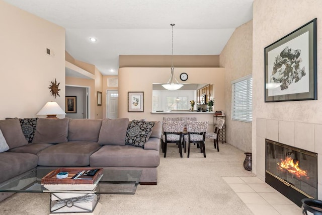 carpeted living room with a tiled fireplace and vaulted ceiling