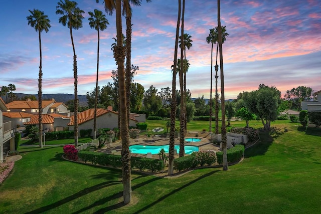 pool at dusk with a patio and a lawn