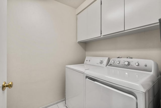 clothes washing area with washing machine and dryer, light tile patterned flooring, and cabinets