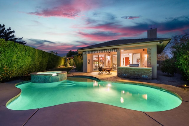 pool at dusk featuring an in ground hot tub and a patio area