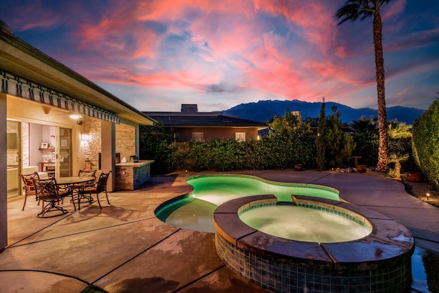 pool at dusk featuring a mountain view, a patio, and an in ground hot tub