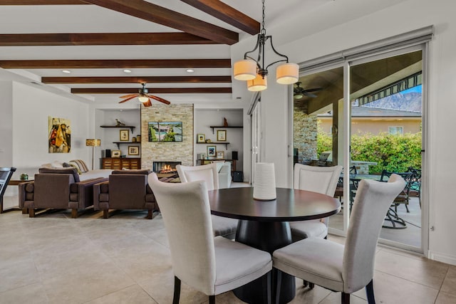 tiled dining space featuring beamed ceiling, ceiling fan with notable chandelier, and a fireplace