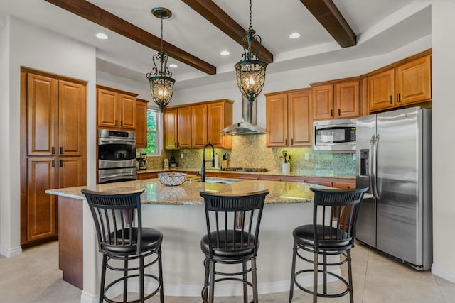 kitchen featuring appliances with stainless steel finishes, an island with sink, wall chimney exhaust hood, beamed ceiling, and an inviting chandelier