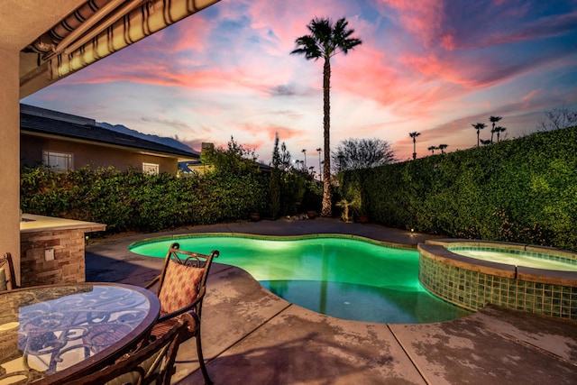 pool at dusk featuring an in ground hot tub and a patio area