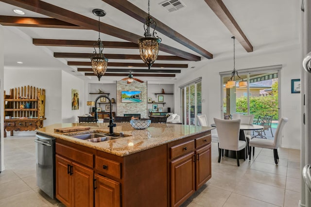 kitchen featuring light stone counters, an island with sink, hanging light fixtures, beam ceiling, and a stone fireplace