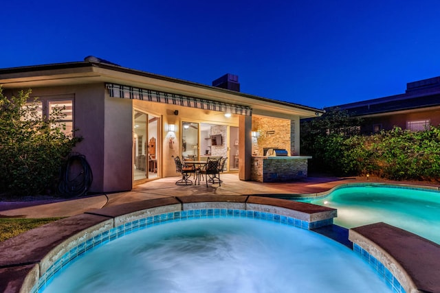 pool at twilight with an in ground hot tub, a patio area, and an outdoor kitchen