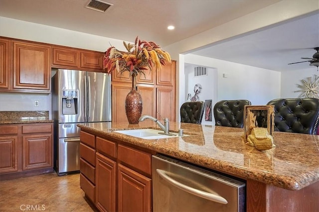 kitchen with sink, stainless steel appliances, light stone counters, an island with sink, and light tile patterned flooring