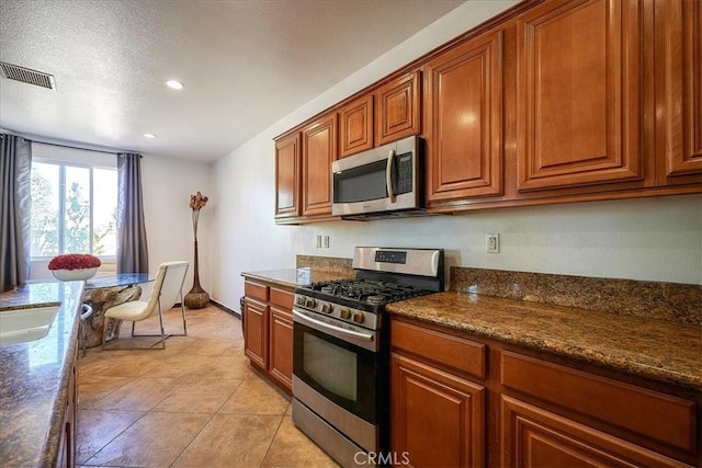 kitchen featuring sink, dark stone countertops, light tile patterned floors, a textured ceiling, and appliances with stainless steel finishes