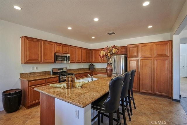 kitchen featuring sink, stainless steel appliances, light stone counters, a breakfast bar, and a center island with sink