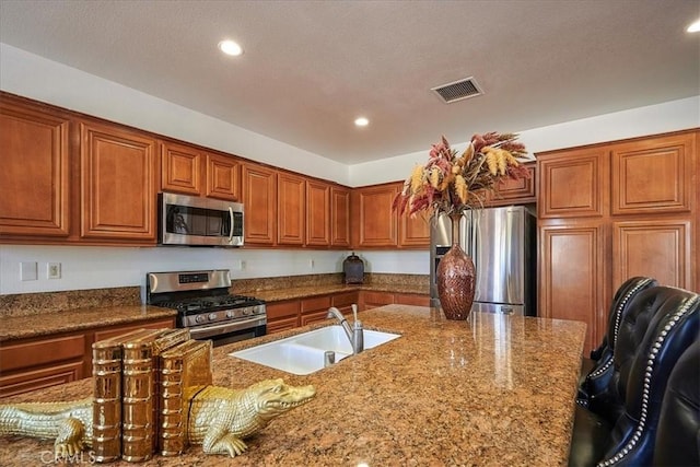 kitchen with a kitchen island with sink, sink, stainless steel appliances, and stone counters