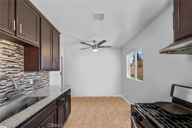 kitchen with dark brown cabinetry, sink, backsplash, light stone countertops, and stainless steel range with gas cooktop