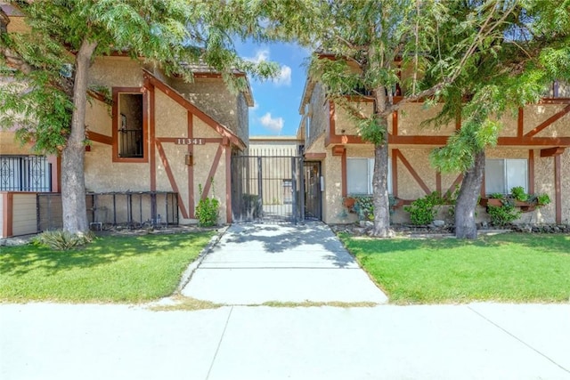 view of front facade with stucco siding, a gate, and a front lawn